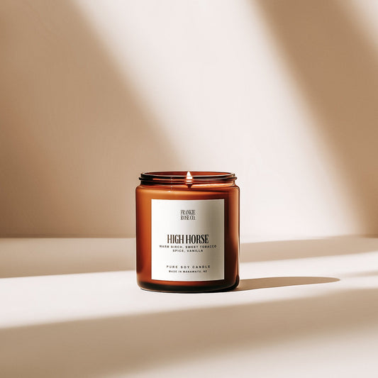 A candle named "High Horse," offering a dark, sensual fragrance with warm birch, sweet vanilla, and spice. The luxurious scent features notes of dried fruit, tobacco blossom, and woody undertones, creating a romantically masculine aroma.